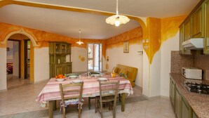 A dining area with a table set for four, a kitchen with green cabinets, and a window with a view. - Apartment "Alloro" with Terraces & Wi-Fi (Sos Alinos)