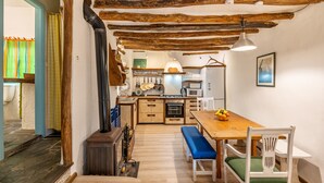 A rustic kitchen with wooden beams, a dining area with a bench, and a visible stove. - Holiday Home 'La Lechuga Azul' with Mountain View, Private Terrace and Wi-Fi (Guejar Sierra)