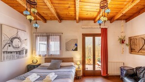 A bedroom with a wooden ceiling, a bed with patterned bedding, a nightstand with a lamp, and a view to an outdoor area. - Holiday Home 'La Lechuga Azul' with Mountain View, Private Terrace and Wi-Fi (Guejar Sierra)