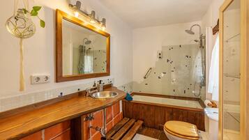 Un baño con tocador de madera, lavamanos, inodoro, bañera y ducha.