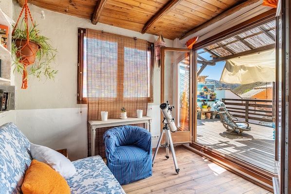 A cozy room with a wooden ceiling, a telescope, a rocking chair, and a view of a deck.