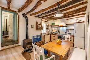 A rustic kitchen with exposed wooden beams, a wooden dining table with chairs, a stove, and modern appliances.