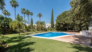 Une piscine entourée d’une pelouse et de grands arbres.