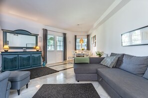 A modern living room with a grey sofa, a dark blue cabinet, and a dining area with a white table and chairs. - Holiday Home 'Karma' with Shared Pool, Wi-Fi and Air Conditioning (mijas)