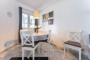 A dining area with a round table, white chairs, a hanging light fixture, and artwork on the wall. - Holiday Home 'Karma' with Shared Pool, Wi-Fi and Air Conditioning (mijas)