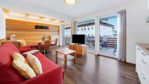 Een moderne woonkamer met een rode bank, houten details, een televisie en een balkon met uitzicht.