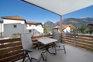 A balcony with a table and chairs, overlooking a mountain range and residential buildings.