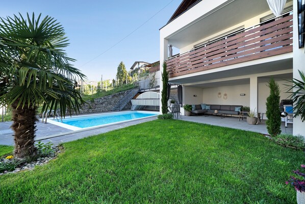 A modern two-story house with a swimming pool, a well-maintained lawn, and a stone staircase leading to a second level.