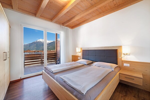 Une chambre avec deux lits, un plafond en bois, une table de chevet et une vue sur les montagnes par la fenêtre.