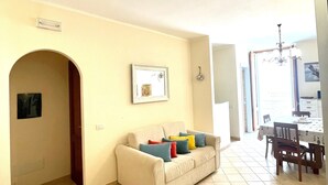A living room with a sofa, a dining table, and chairs. There is a doorway leading to another room.