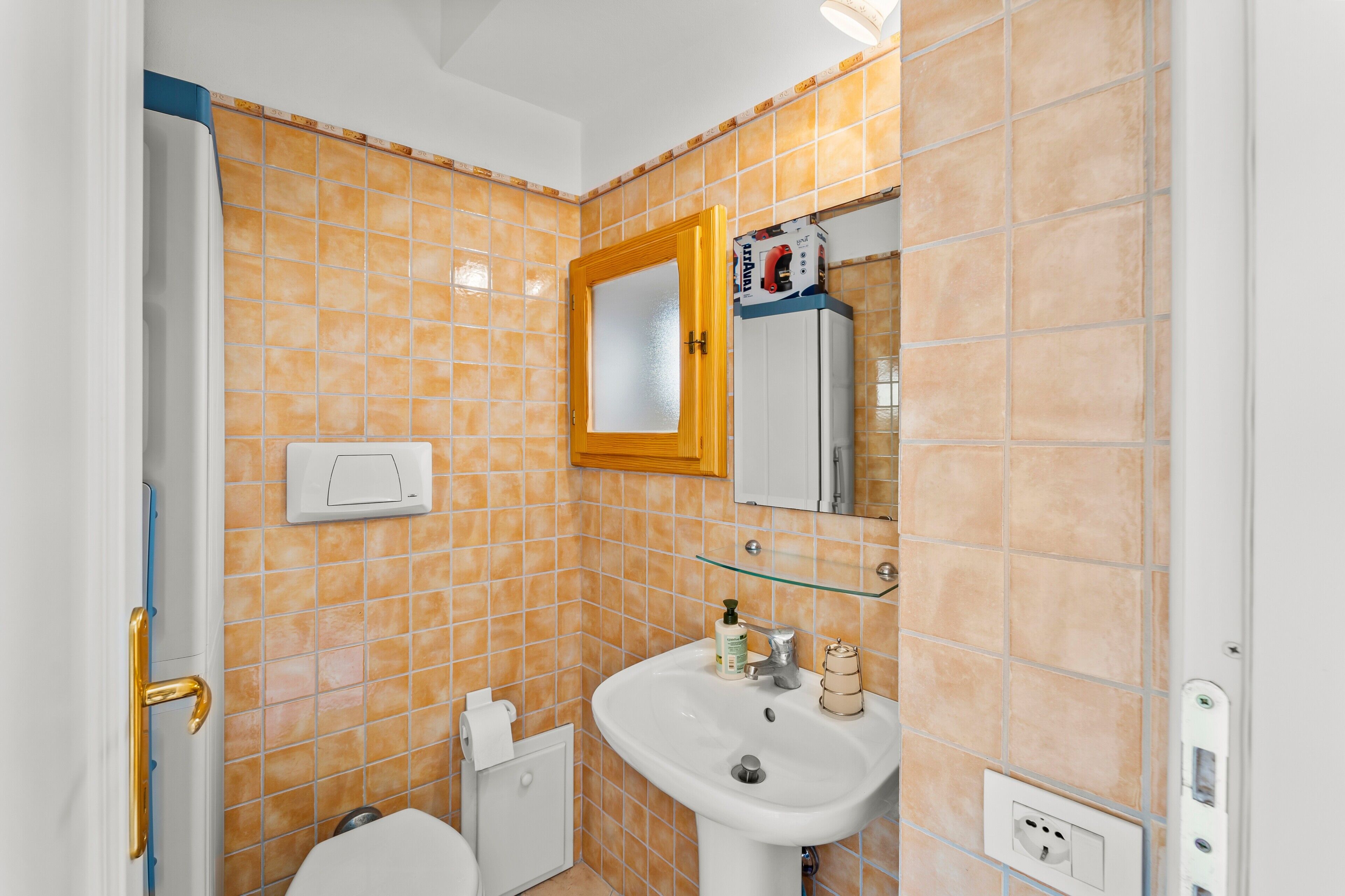 Casa de banho com lavatório branco, espelho em cima e parede revestida a azulejos.