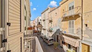 A narrow street with buildings on either side, a parked car, and a small tree.