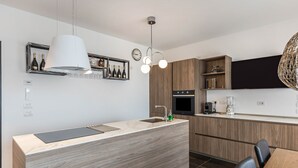 Una cucina moderna con isola centrale, mobili in legno, forno incassato e lampadario a sospensione.