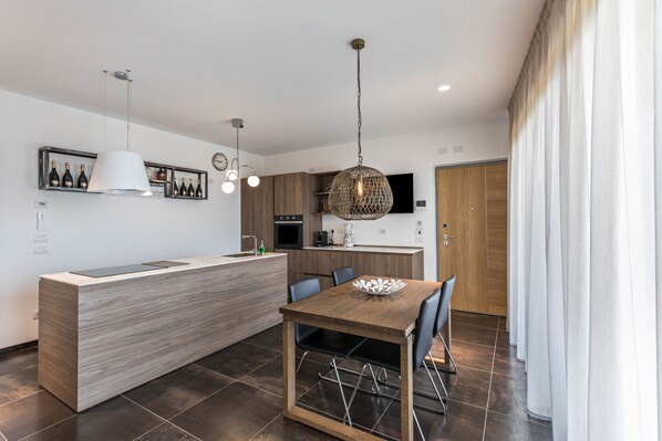 A modern kitchen with a central island, pendant lighting, and a dining area with chairs.