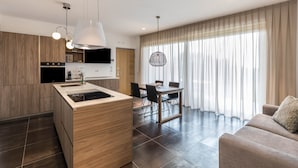 Una cucina moderna con isola centrale, zona pranzo con sedie e divano in un soggiorno con ampie finestre.