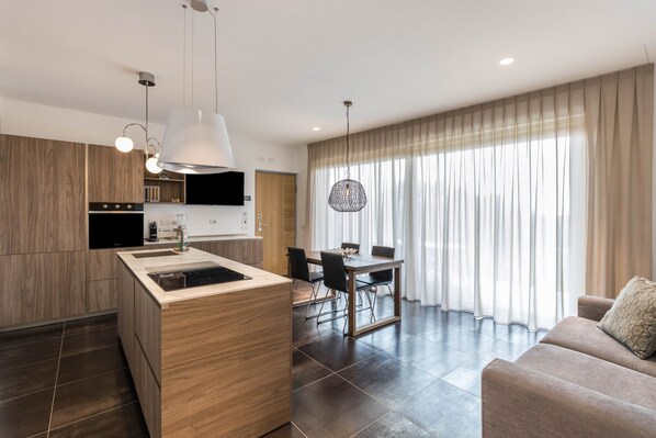 A modern kitchen with a central island, dining area with chairs, and a sofa in a living room with large windows. - Apartment "Bardolino Luxury - Ground Floor" with Lake View (bardolino)