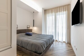 A modern bedroom with a bed, a mounted TV, and a large window with curtains.