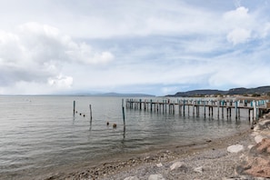 A calm lake with a wooden pier extending into the water, surrounded by rocky shores and distant hills.