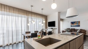 Eine moderne Küche mit einer zentralen Kochinsel, Essbereich und Wohnbereich mit Flachbildfernseher und Kunstwerken.
