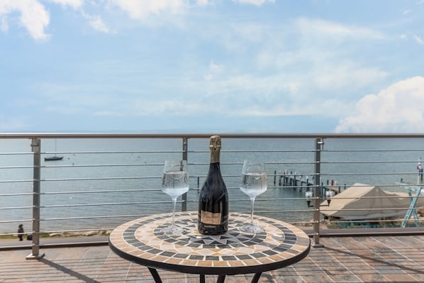 A table with a bottle of champagne and two glasses on a tiled patio overlooking a body of water.