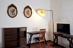 A room with a wooden desk, a chair, a television, and two framed pictures on the wall.