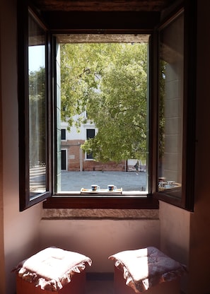 Une chambre avec une fenĂȘtre, deux tables de chevet et une vue sur un arbre et des bĂątiments Ă lâextĂ©rieur.
