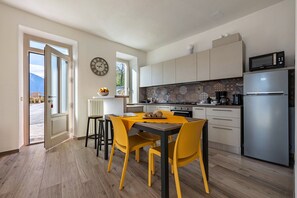 A modern kitchen with a dining area, featuring a large window, a clock, and a refrigerator. - Apartment 'Casa Bepi' with Lake View, Private Terrace and Wi-Fi (Tremosine sul Garda)