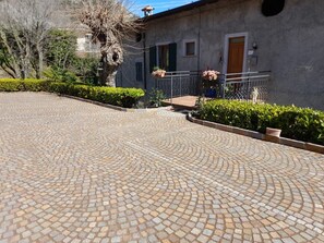 A paved courtyard with a stone floor, a building with a door and windows, and a tree with hanging plants. - Apartment 'Casa Bepi' with Lake View, Private Terrace and Wi-Fi (Tremosine sul Garda)