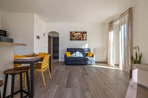 A living room with a sofa, a dining table with chairs, a painting on the wall, and a window with curtains. - Apartment 'Casa Bepi' with Lake View, Private Terrace and Wi-Fi (Tremosine sul Garda)