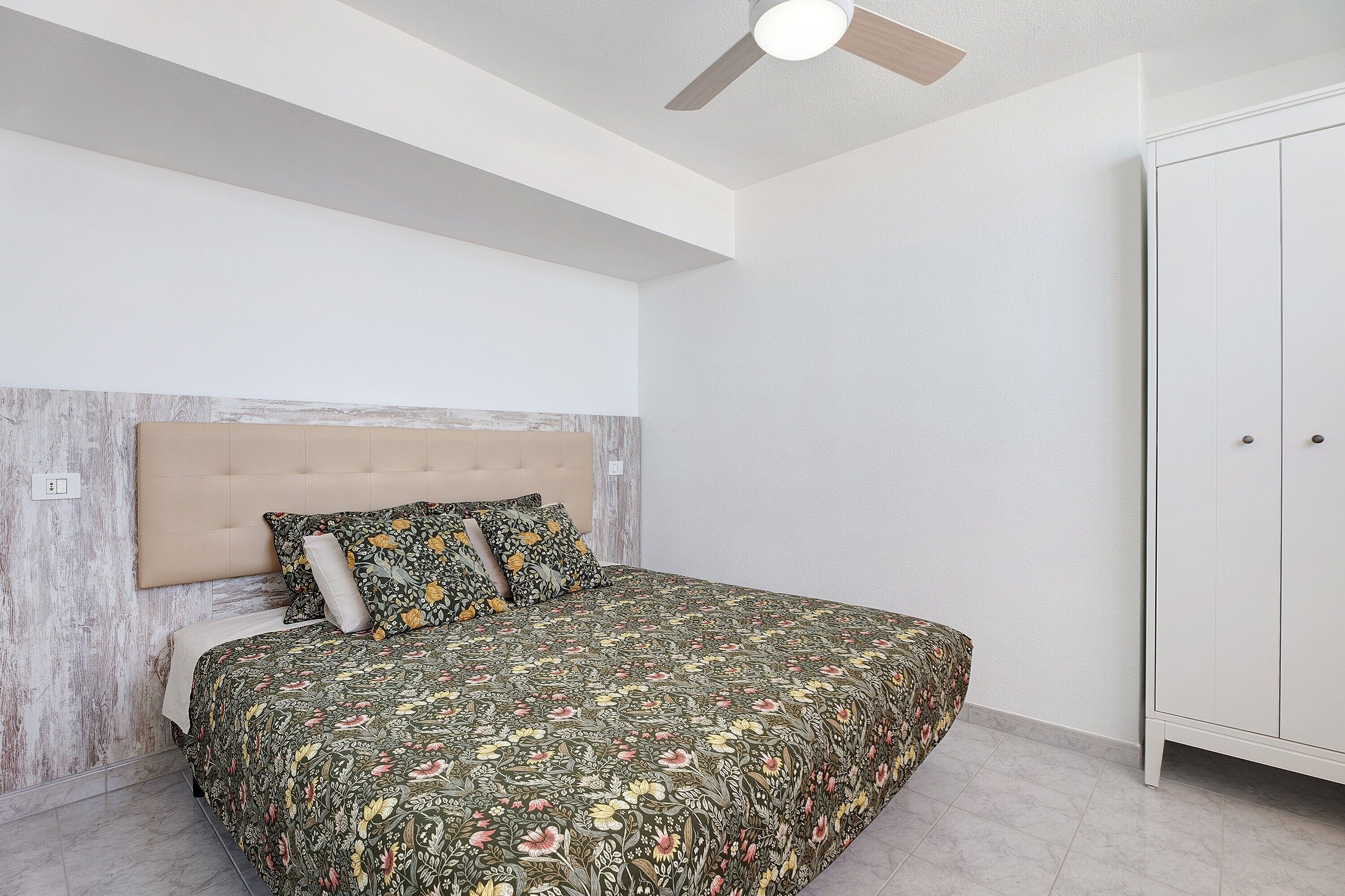 A bedroom with a bed, a ceiling fan, and a wardrobe.