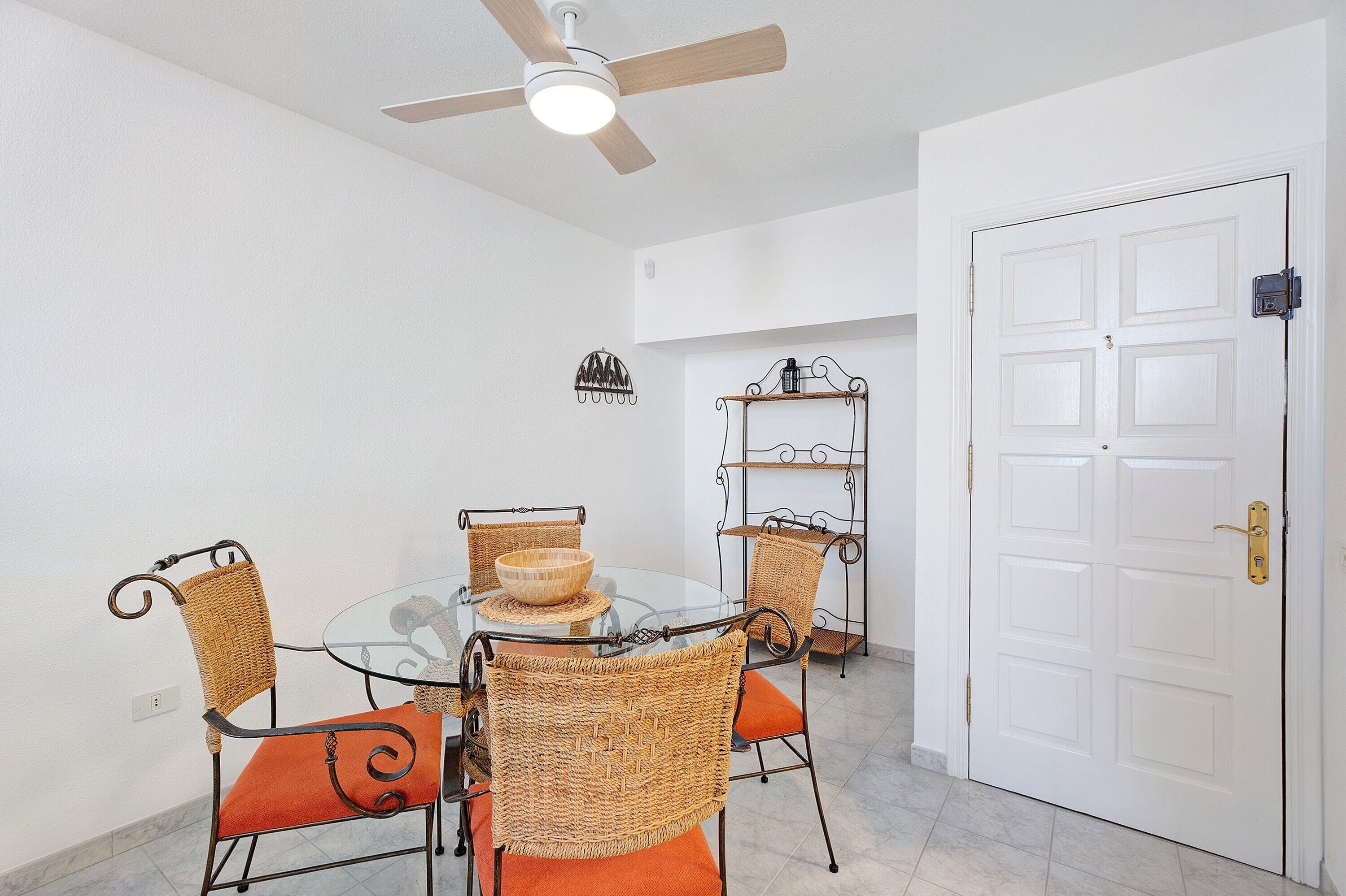 A dining area with a glass table, wicker chairs, and a ceiling fan.