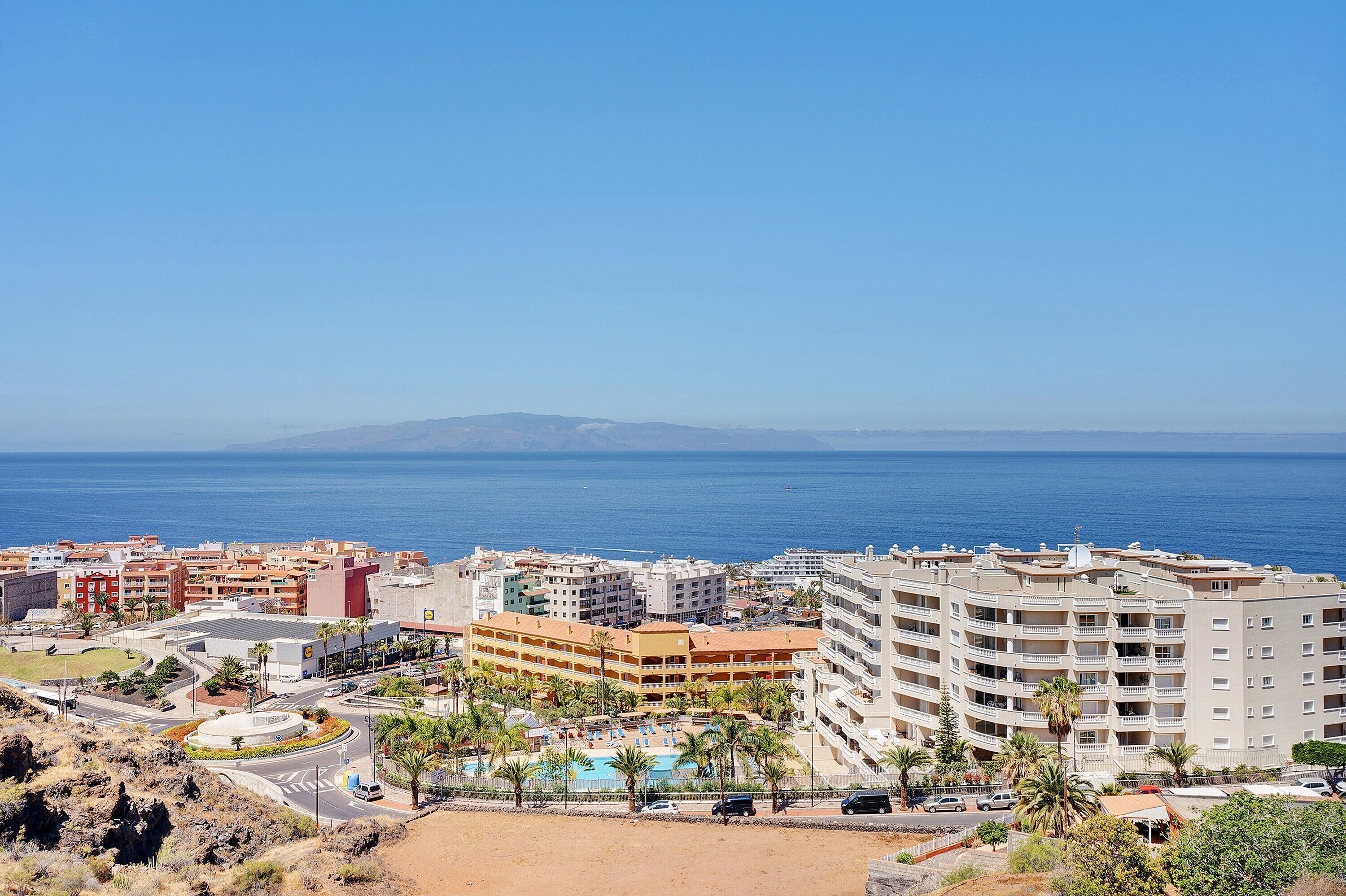 A coastal hotel with multiple floors, a swimming pool, and a view of the sea.
