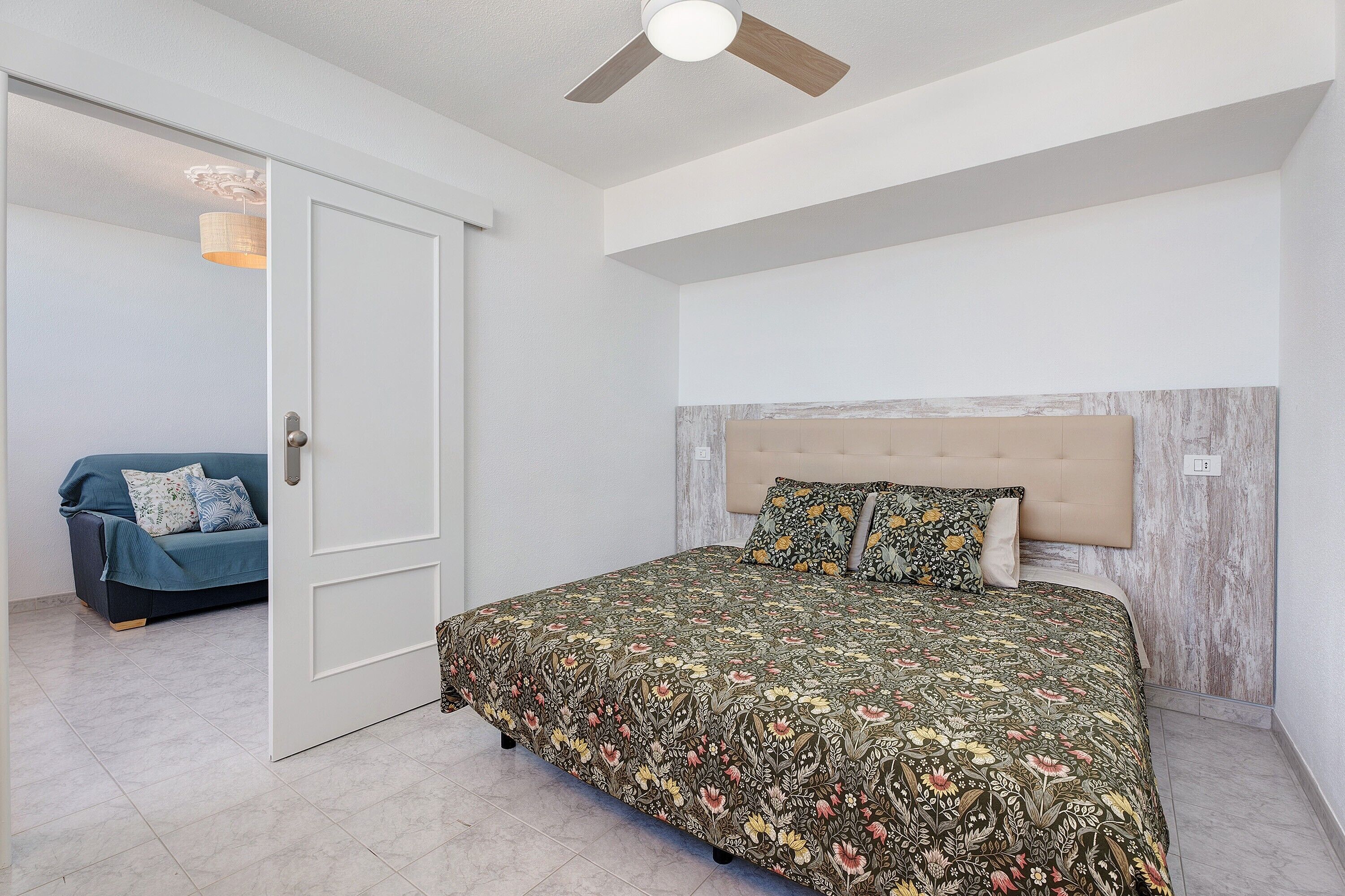 Une chambre à coucher avec un lit, un ventilateur de plafond et une porte donnant sur une autre pièce.