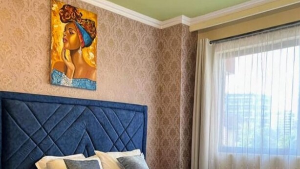 Quarto com cama grande, cabeceira, quadro na parede e janela com cortinas.