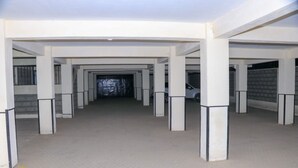 Vários pilares brancos com bases pretas, chão de concreto e um carro estacionado ao fundo.
