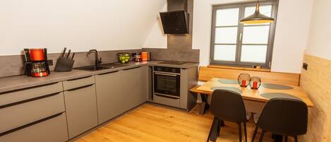 A modern kitchen with grey cabinets, a wooden dining table with black chairs, and a window with a view.