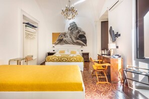 A hotel room with two beds, a desk, a chair, a chandelier, a large painting, and a TV. - Terra d'Amuri Hotel (Catania)