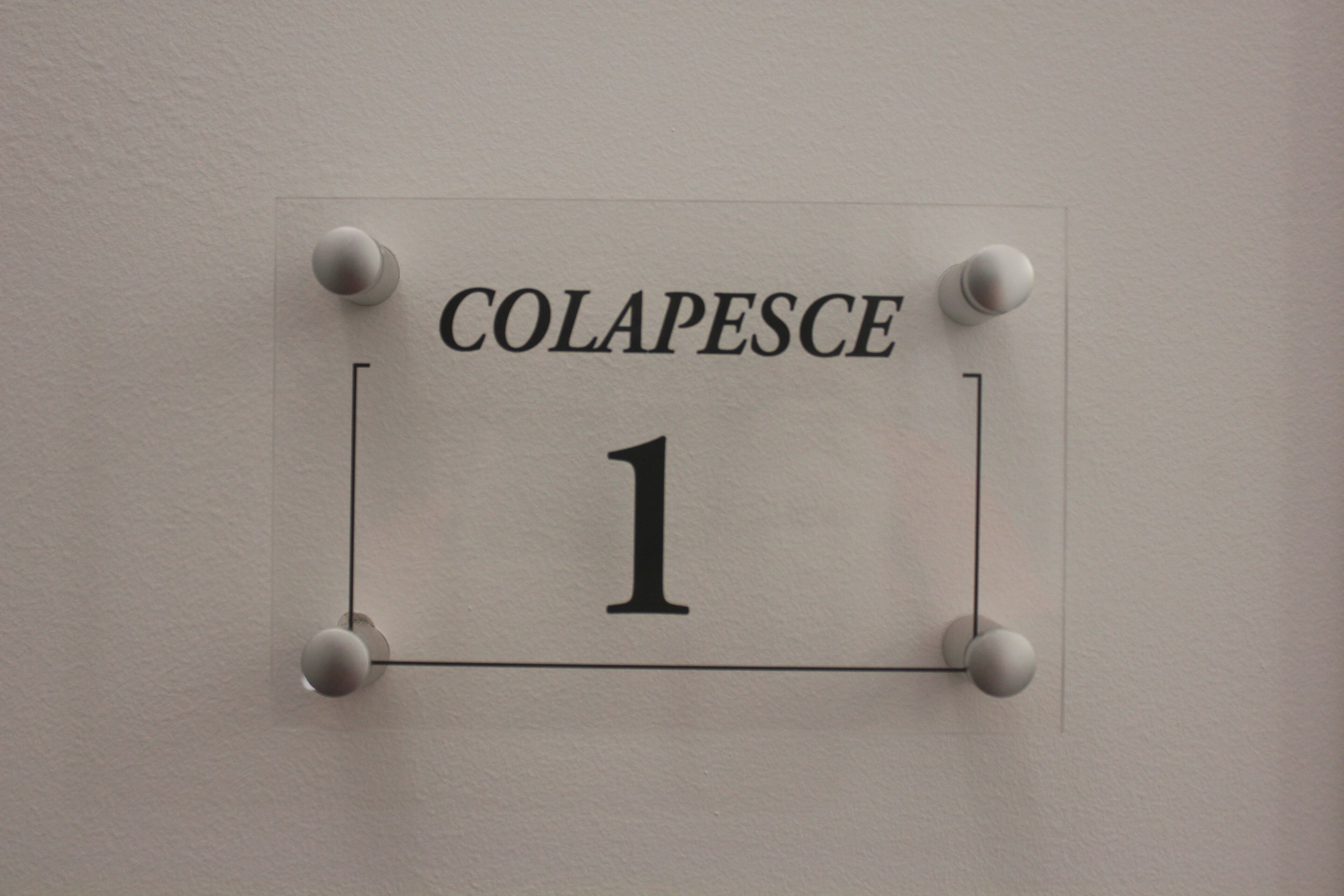 Un letrero con el texto 'COLAPESCE 1' sujeto a una pared.