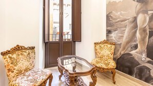 A room with two ornate chairs, a glass-top table, and a large painting of a figure on the wall. - Terra d'Amuri Hotel (Catania)