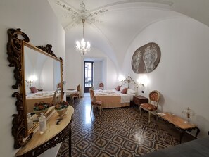 A room with a large ornate mirror, a chandelier, a bed with a headboard, a table with a vase of flowers, and a patterned floor. - Terra d'Amuri Hotel (Catania)