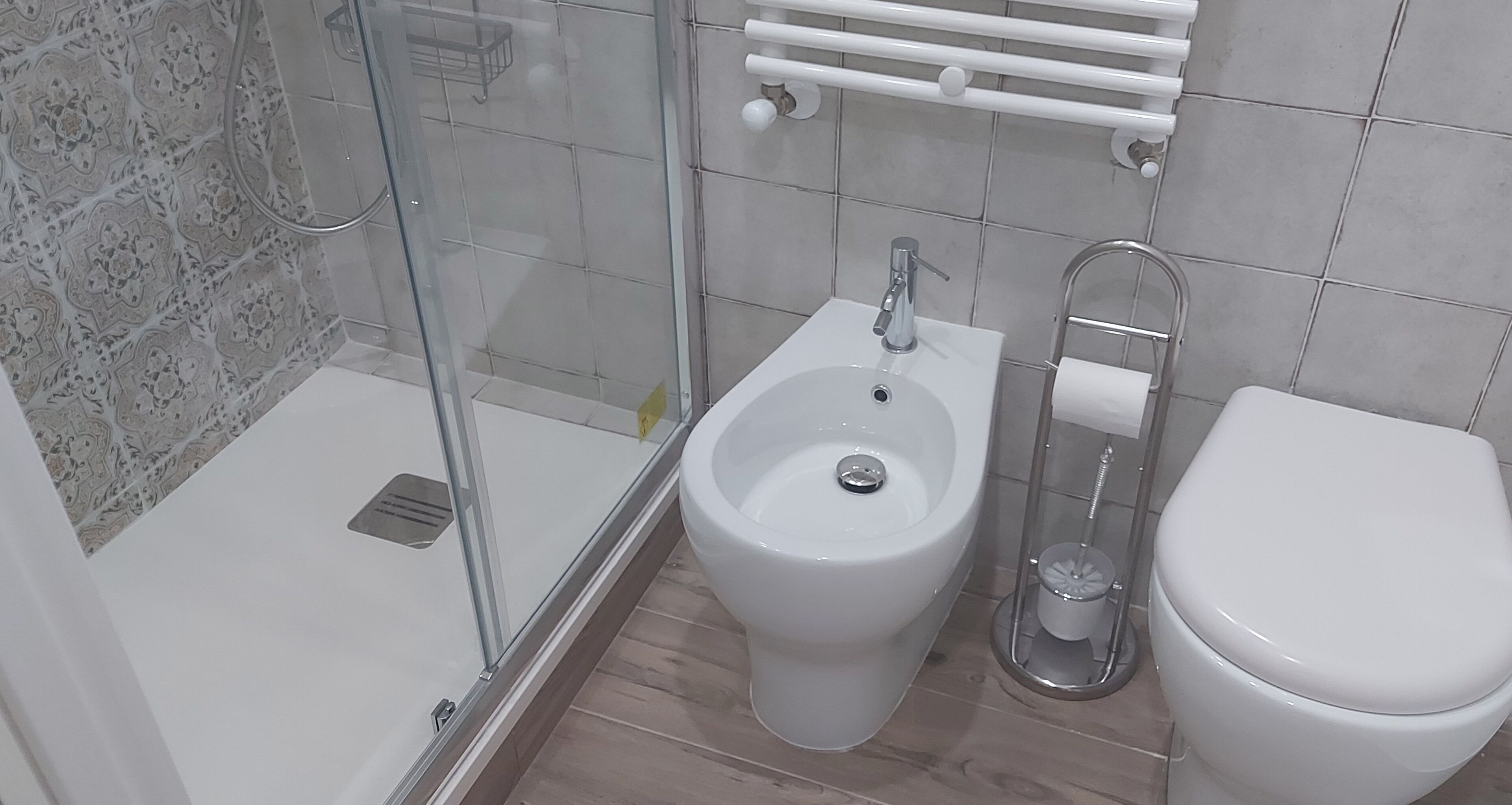 Un baño con cabina de ducha de vidrio, lavamanos pedestal, inodoro y toallero.