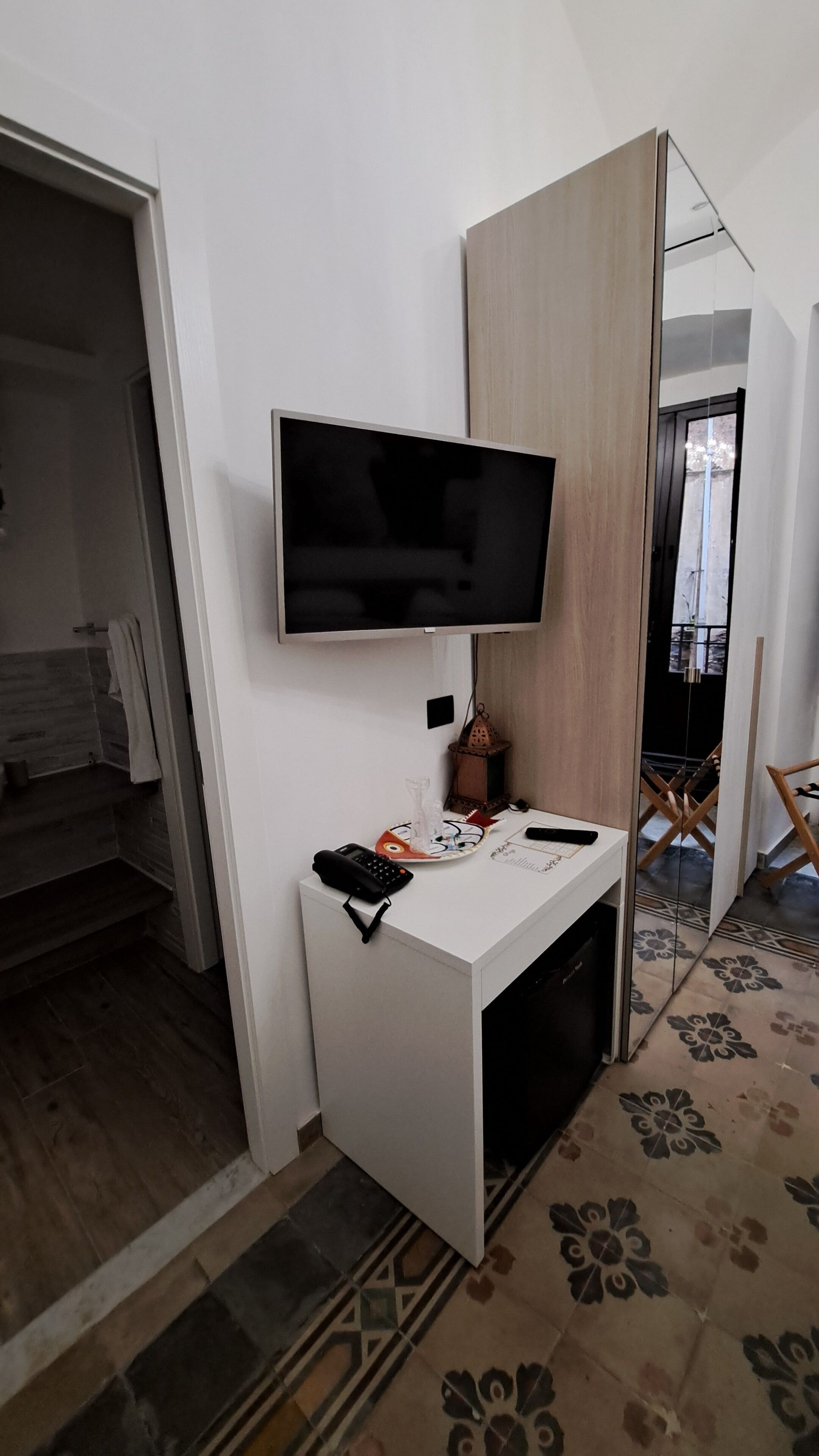 Un baño moderno con un tocador blanco, un televisor montado y un espejo.
