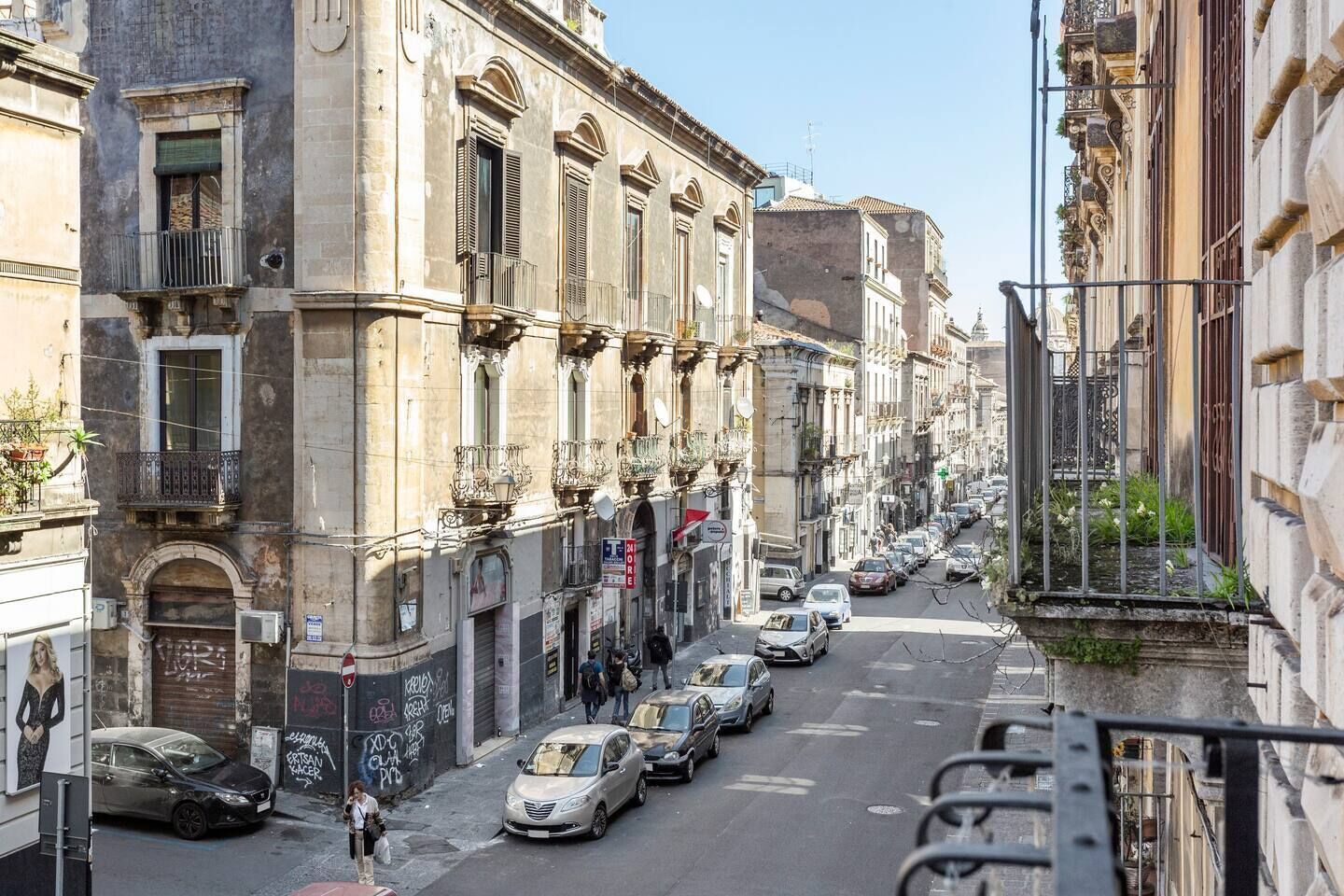 A street lined with historic buildings, parked cars, and pedestrians.