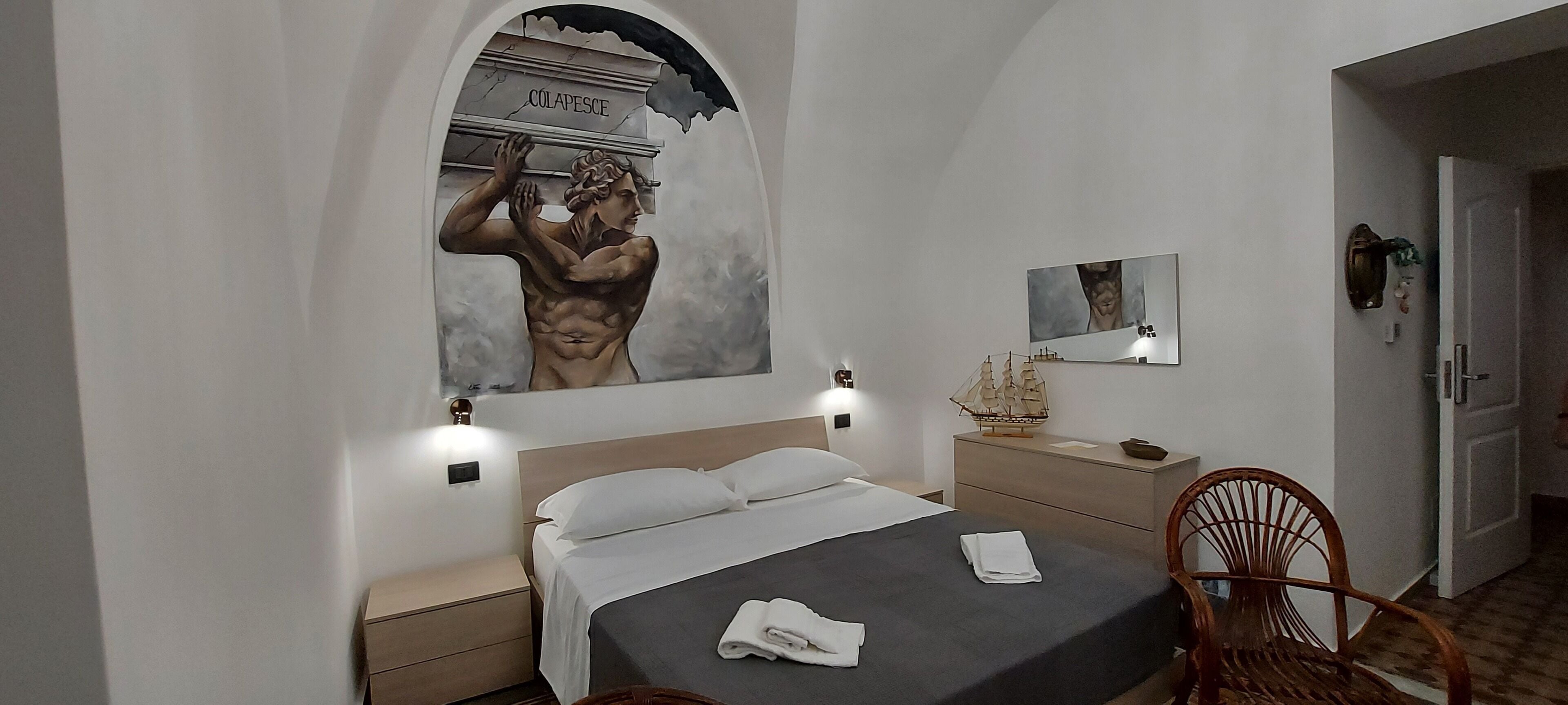 A hotel room with a bed, a nightstand, a chair, a dresser, a mirror, and a wall mural.