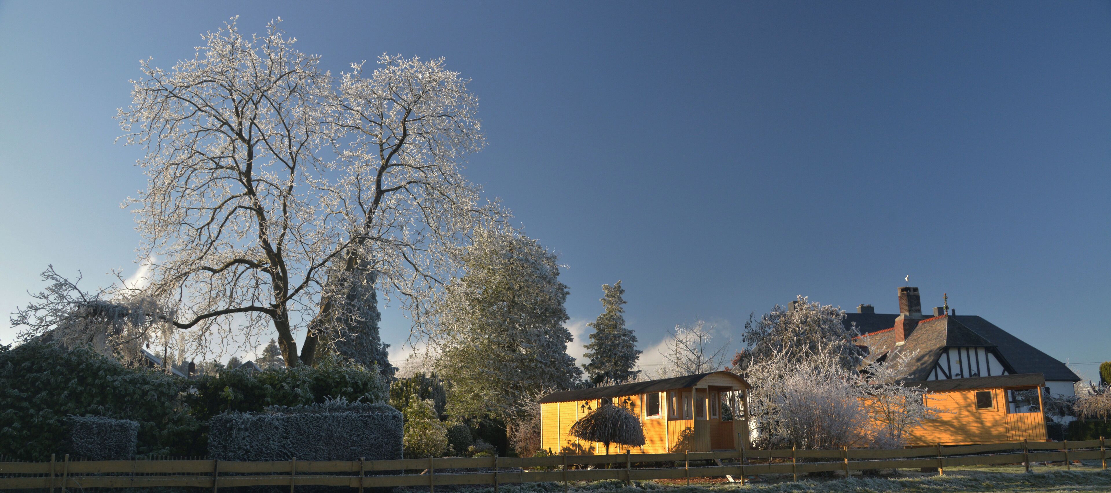 Una casa tradicional amb estructura de fusta i rajola, envoltada d'arbres coberts de neu i una tanca de fusta.