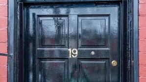 Una puerta negra con el número 19, un picaporte y un cerrojo de latón.