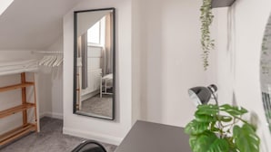 Una habitación con un espejo grande, un estante de madera, un radiador y una planta.