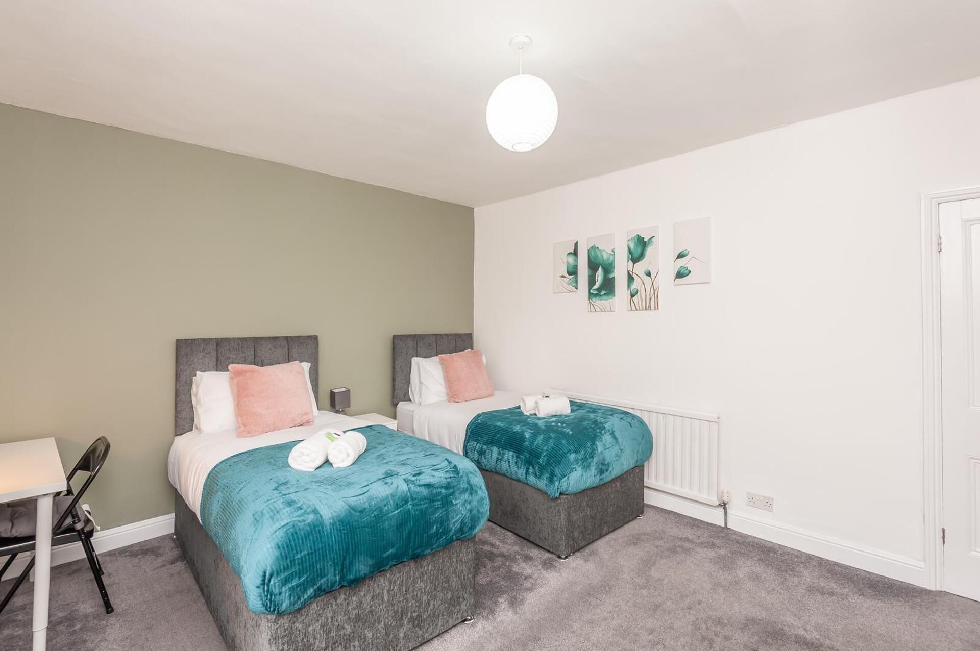 A bedroom with two beds, a desk, and a chair. There are wall art pieces and a door.
