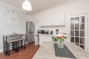 A modern kitchen with white cabinets, a stainless steel refrigerator, a dining area with a table and chairs, and a vase with flowers on the counter.