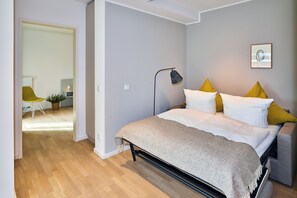 Un dormitorio con cama, lámpara de noche y vista a otra habitación.